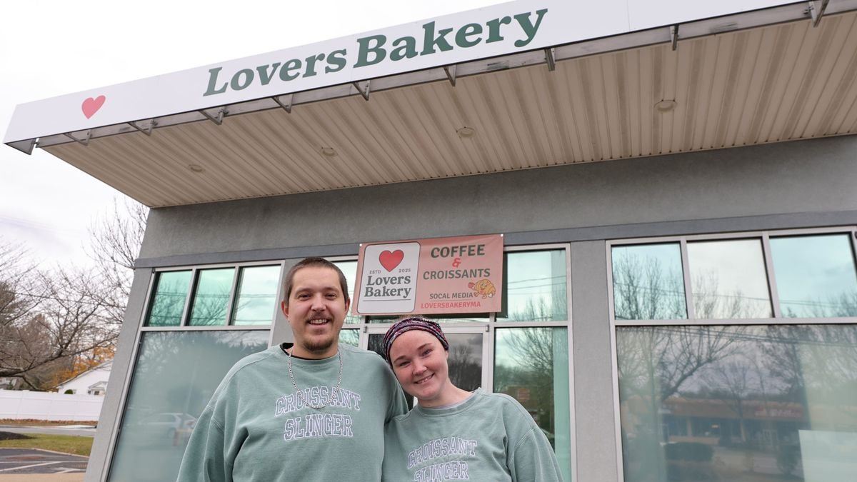 Allie and Jake smiling outside Lovers Bakery, wearing matching gray shirts that say 'Croissant Slinger'.