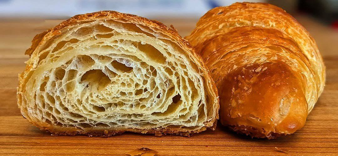 Close-up of a flaky croissant with a crispy golden-brown exterior, cut in half to show its layered, airy interior.