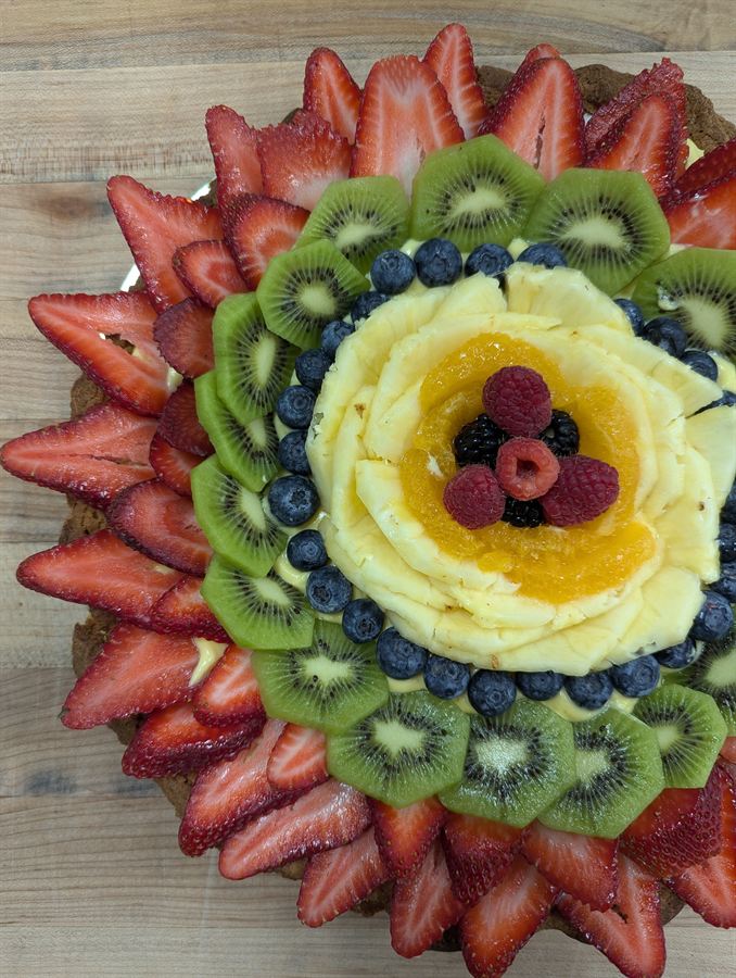 Fruit tart topped with rings of sliced strawberries, kiwi, blueberries, and pineapple