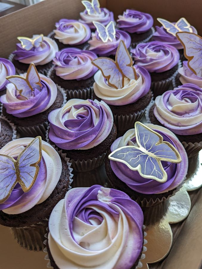 Box of cupcakes with purple rose frosting and gold-trimmed butterfly toppers